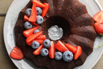 Tasty chocolate bundt cake with berries on wooden table, top view