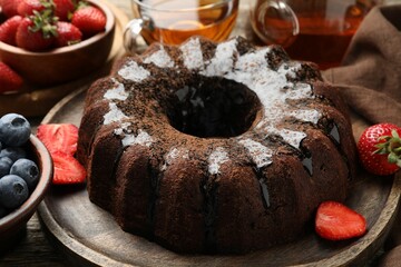 Tasty chocolate bundt cake with glaze, tea and berries on wooden table, closeup