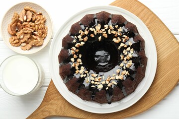 Delicious chocolate bundt cake with nuts and glass of milk on white wooden table, flat lay