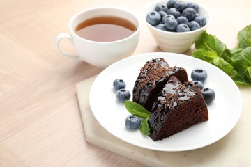 Pieces of delicious bundt cake with blueberries, mint, chocolate shavings and tea on wooden table, closeup