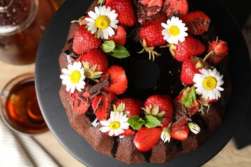 Delicious chocolate bundt cake with strawberries, mint and chamomile flowers on table, top view