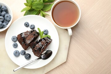 Pieces of delicious bundt cake with blueberries, mint, chocolate shavings and tea on wooden table, flat lay. Space for text