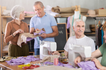 During lesson in sewing studio, elderly participants communicate and discuss execution of...