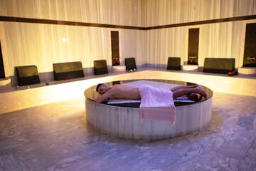 Man relaxing on a marble platform inside a Turkish bath with warm lighting.