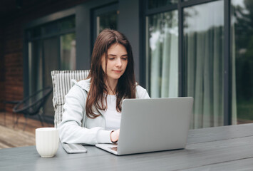 Young woman working on a laptop outdoors with a smartphone and coffee. Remote work, focus, and modern lifestyle concept.