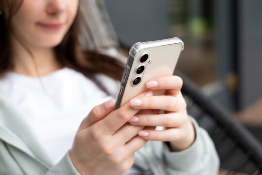 Young woman using Samsung Galaxy S23 FE smartphone indoors, browsing or texting in a relaxed and modern environment.