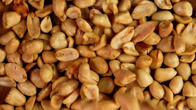 Top view slow motion of Peeled salted fried peanuts falling into a wooden plate on a black background. Suitable for advertising or promotion.