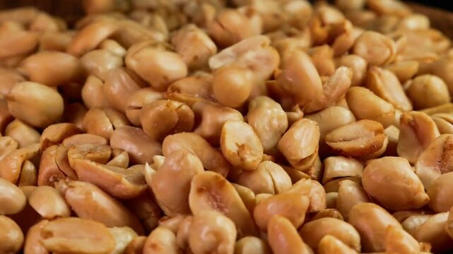 Slow motion of Peeled salted roasted peanuts falling into a rotating wooden plate. Suitable for advertising or promotion.
