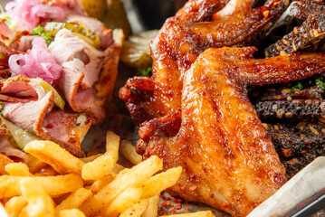 Close-up of a delicious meal featuring crispy chicken wings, sliced roast pork with pickles and onions, seasoned French fries, and grilled meat.