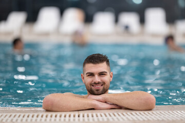 Man resting on the edge of a large indoor pool with a calm expression and relaxed posture.