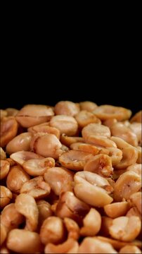 Detail of roasted peanuts peeled rotating on black background. Suitable for advertising or promotion. Vertical shot