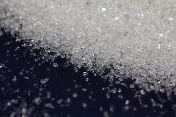 Heap of pure white granulated sugar crystals glittering under bright light against a dark background, illustrating concepts of sweetness, diet, and nutrition