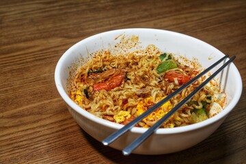 Close-up of a serving of Asian spicy noodles with shrimp and egg in a white bowl, ready to eat.