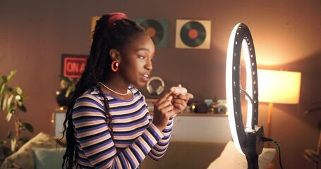 Influencer, ring light and black woman live streaming with makeup for social media, review or night. Content creator, recording and talking to followers for cosmetics brand sponsor and promo in home