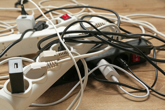 Extension power boards overloaded with plugs on wooden floor, closeup