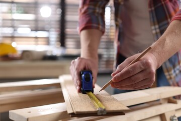 Man measuring wooden plank with tape and pencil indoors, closeup