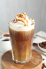 Tasty iced coffee with whipped cream, syrup and beans on white table