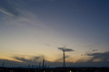 Fototapeta premium Moody Gray Twilight Sky with Silhouetted Power Lines and Pylons Over a Dark Cityscape