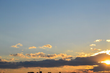 Bright Yellow Sunburst Peeking Through Dark Clouds Over a Silhouetted Blue Cityscape