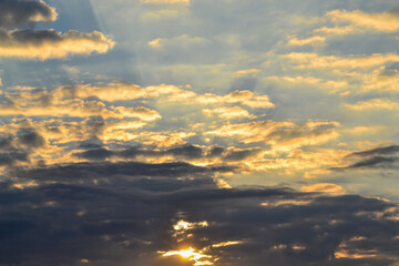 Heavenly Blue and Yellow Sky with Sun Beams Radiating from Behind Dark Gray Clouds