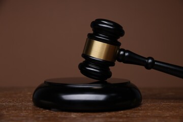 Judge's gavel and sound block on wooden table against brown background, closeup