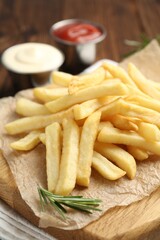 Tasty french fries served with sauces and rosemary on wooden table, closeup