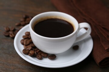 Aromatic coffee in cup, beans and saucer on wooden table, closeup