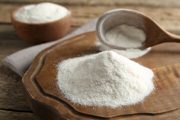 Wheat flour and spoon on wooden table, closeup