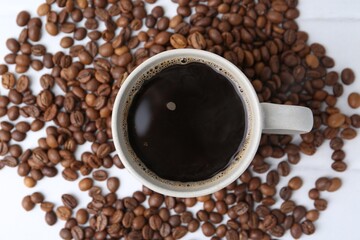 Aromatic coffee in cup and beans on white table, top view