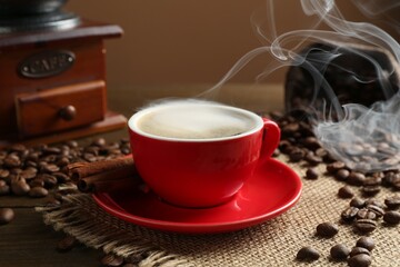Aromatic coffee in cup, beans, cinnamon and grinder on wooden table, closeup