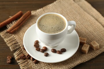 Aromatic coffee in cup, beans, brown sugar and cinnamon on wooden table, closeup