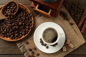 Aromatic coffee in cup, beans, brown sugar and grinder on wooden table, flat lay