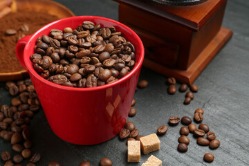 Aromatic coffee beans in cup, grinder and brown sugar on black table, closeup