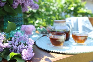 Beautiful lilac flowers, sweets and tea on wooden table in garden, closeup