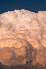Massive cumulus cloud formation illuminated by golden sunset light. Majestic cotton-like cloud against deep blue sky, creating a dramatic natural sculpture in the atmosphere..