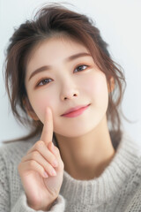 Beautiful asian woman with finger on cheek smiling gently isolated on white background