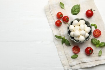 Tasty mozzarella cheese balls, tomatoes and basil on white wooden table, flat lay. Space for text