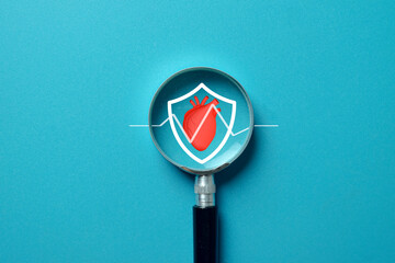 Magnifying glass focusing on a shield with a red heart and ECG line. Concept of heart health,...