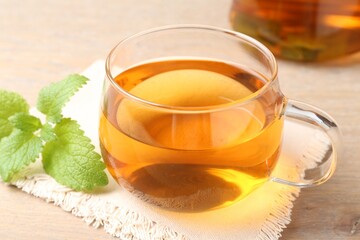 Aromatic lemon balm tea in glass cup and fresh leaves on table, closeup