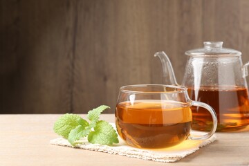 Aromatic lemon balm tea in glass cup, teapot and fresh leaves on wooden table, space for text