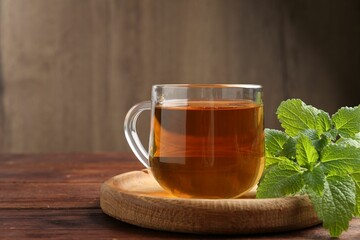 Aromatic lemon balm tea in glass cup and fresh leaves on wooden table, space for text