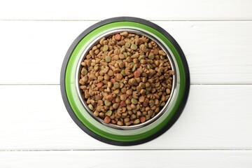 Dry pet food in feeding bowl on white wooden background, top view