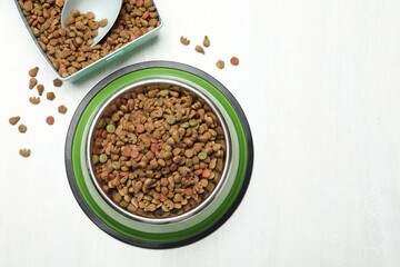 Dry pet food in feeding bowl, container and scoop on light background, flat lay. Space for text