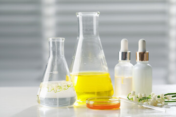Making luxury perfume. Essential oils in glassware and flowers on white wooden table, closeup