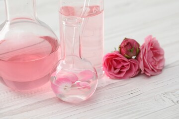 Making luxury perfume. Essential oils in glassware and flowers on white wooden table, closeup