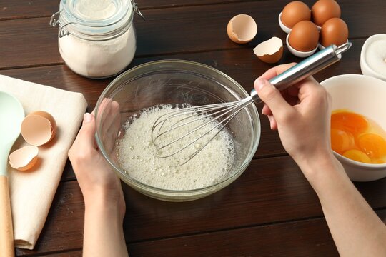 Woman whisking egg whites in bowl at wooden table, closeup