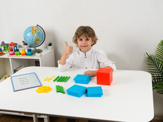 A young boy with short, brown hair is intently focused on a colorful array of base-10 blocks,...