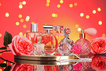 Many different perfume bottles, accessories and flowers on mirror surface against red background with blurred lights, closeup
