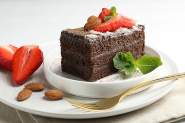 Piece of delicious chocolate cake with strawberries, almonds and mint on table, closeup