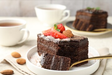 Piece of delicious chocolate cake with strawberry, almonds and tea on table, closeup